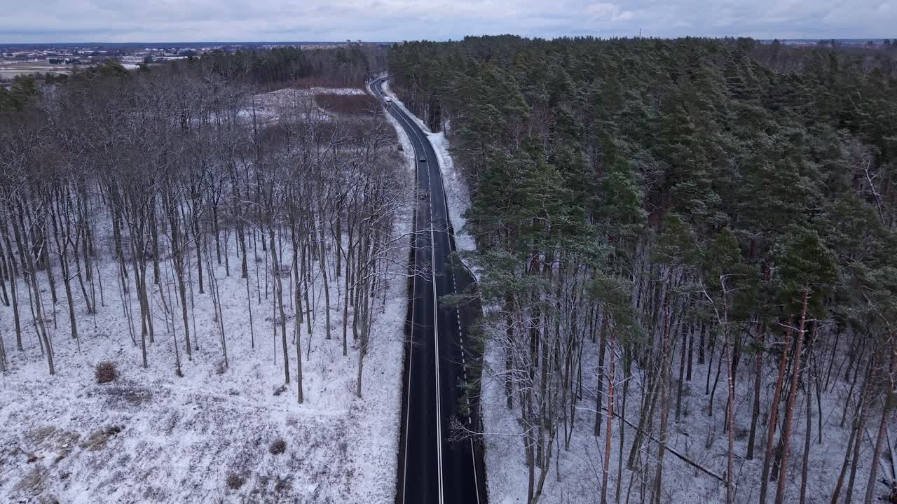 Cars driving through asphalt concrete road surrounded with large pine forest fields in winter snowfall, Road from Elk to Olsztyn, Panoramic drone view, Establishing