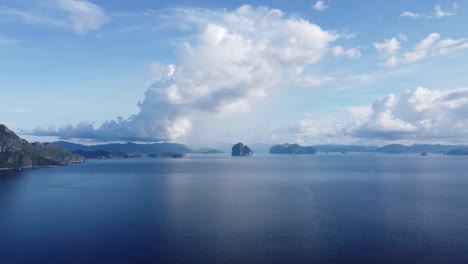 aerial panning view : tropical seascape horizon of small limestone sea mount islands scattered in background under interesting formation of large puffy white clouds and blue sky