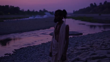 indian sadhu wearing traditional clothes and rudraksha mala beads meditating near river at sunset in rishikesh, india, creating a serene and spiritual atmosphere