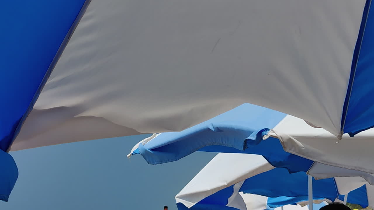 Ombrelloni blu ondeggiano dolcemente sulla spiaggia di Candolim, Goa, al rallentatore.
