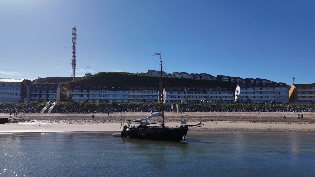 Avvicinamento ravvicinato e a bassa quota di un drone sull'acqua verso una barca a vela a fondo piatto nella baia di Helgoland.