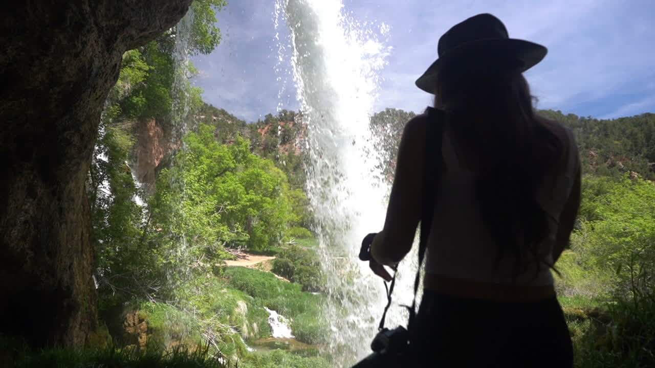 parte posterior de una mujer caminando en una cueva bajo una cascada escénica en un día soleado de verano