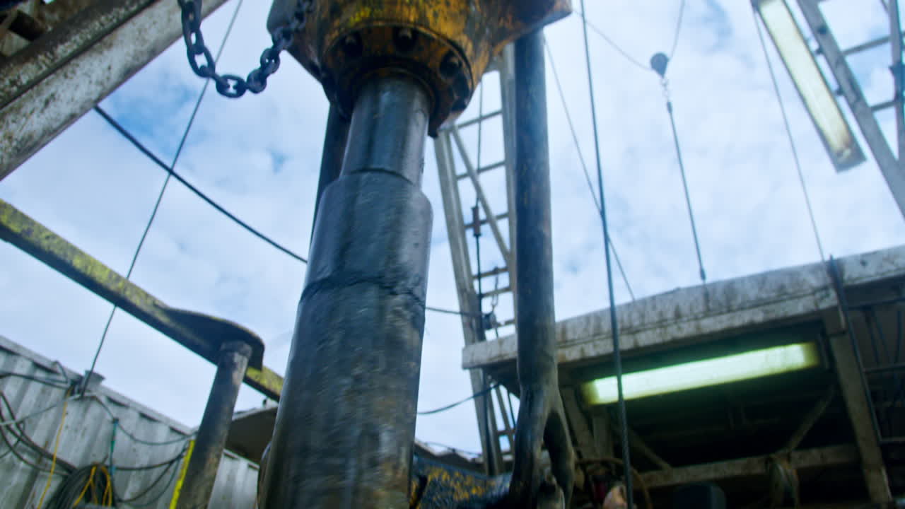 Rotating detail of a drilling equipment attached to the high metal support. Low angle view on the machines for oil or gas production.