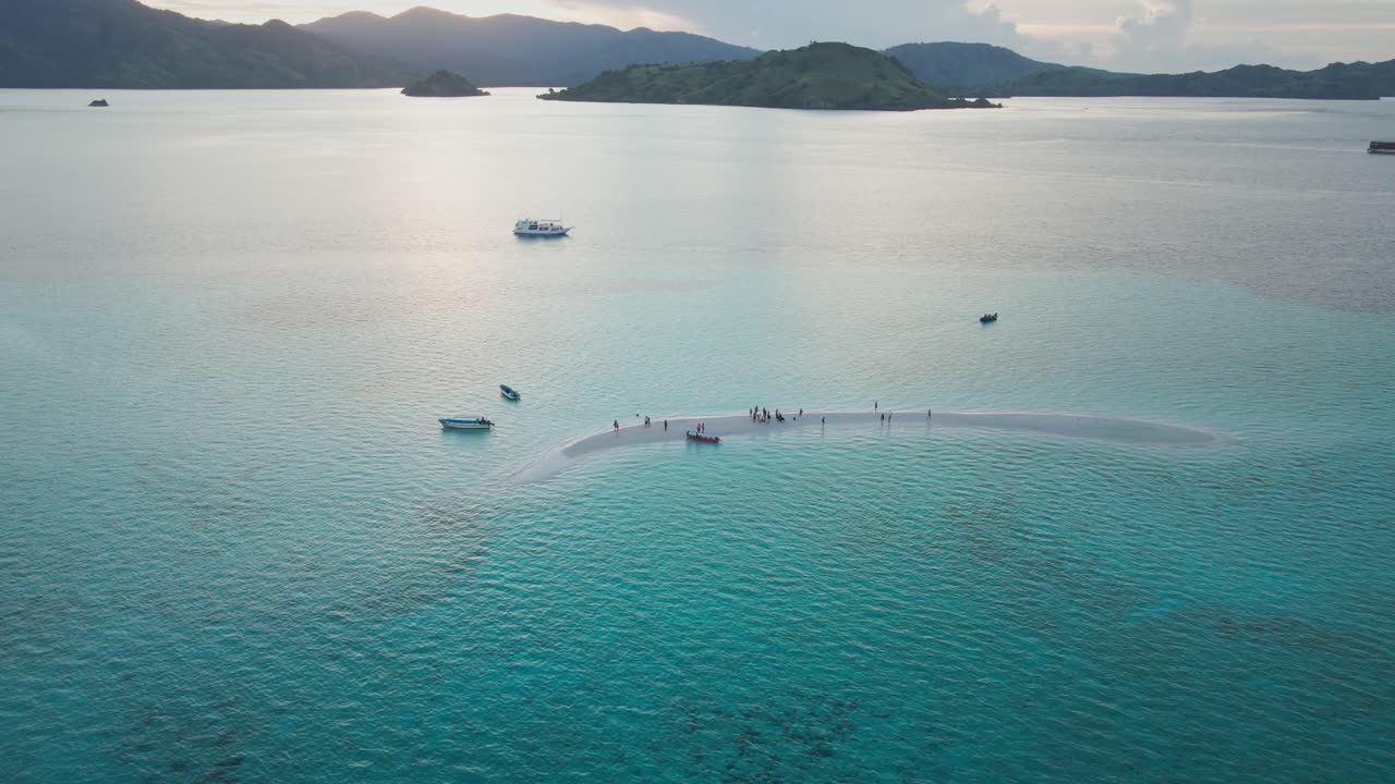 Crystal white sandbar in the middle of the Komodo National Park sea, Flores, surrounded by crystal-clear turquoise water with silhouetted small islands as the backdrop.