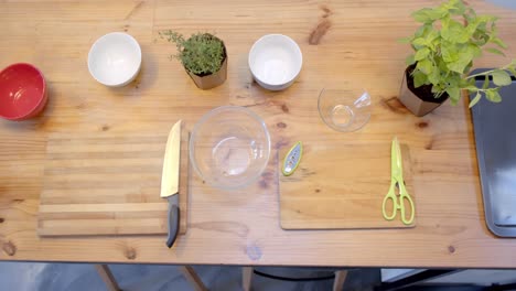 Overhead-view-of-bowls,-cutting-boards-and-knife-on-wooden-table-in-kitchen,-slow-motion