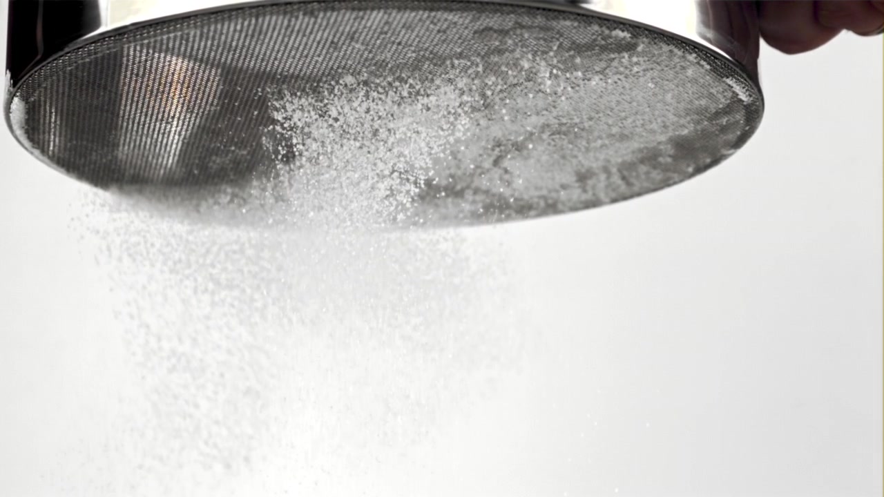 Primer plano de polvo blanco tamizándose a través de un tamiz de metal