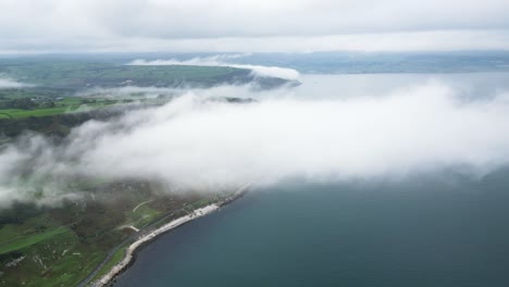 aerial dolly forwards shot from the historic coastal road near glenarm town in northern ireland with view of the blue sea, the beautiful island with nature and clouds