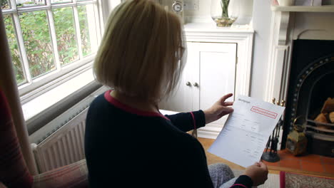 una anciana irreconocible preocupada por las deudas abriendo una carta de deuda