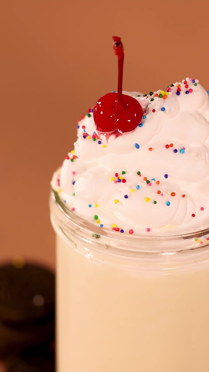 Primo piano lento di milkshake alla vaniglia in un barattolo di vetro con panna montata, codette e guarnizione di ciliegia