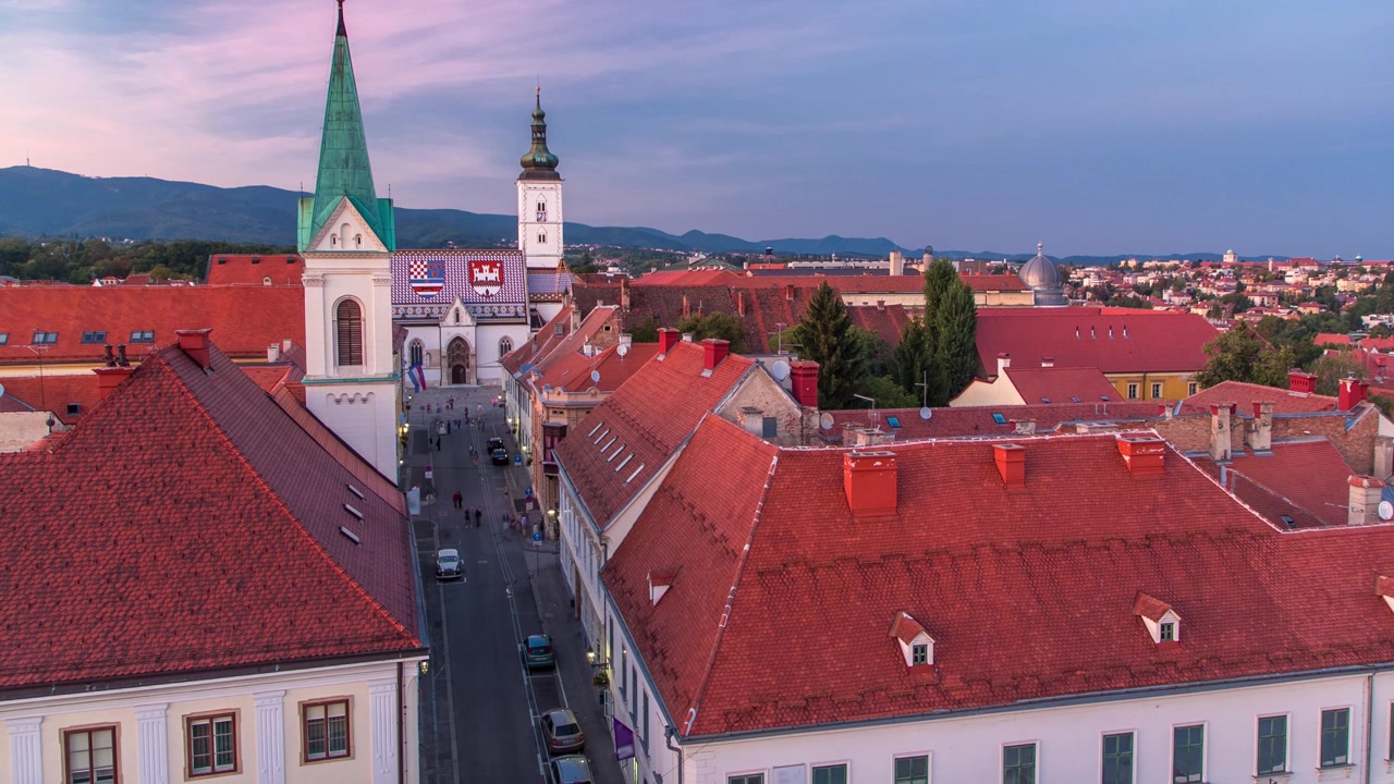 Kościół św. Marka, timelapse przejścia z dnia w noc i budynek parlamentu, Zagrzeb, Chorwacja. Widok z góry z punktu widokowego wieży Kula Lotrščak po zachodzie słońca.