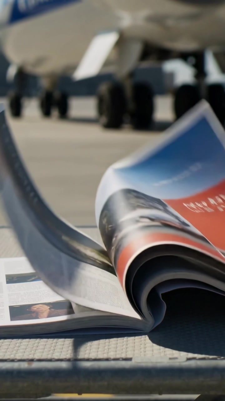 Vidéo verticale : Le vent agite les pages d'un magazine à couverture souple sur une aire de trafic, près d'un train d'atterrissage.