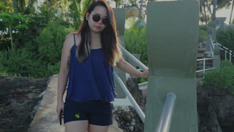 Front-view-of-a-girl-walking-at-Taga-beach-while-holding-the-hand-railing-during-a-bright-morning,-slow-motion