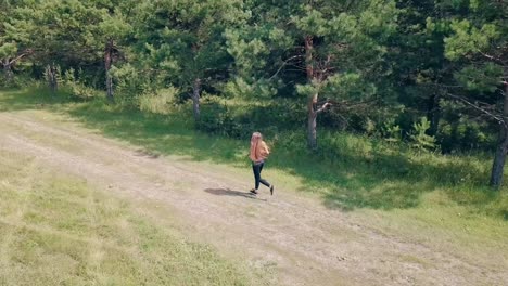 aerial shot tracking young pretty girl goes in for sports in the morning runs along pine forest