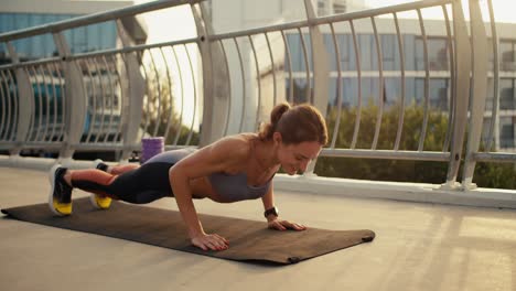 happy girl in a special summer uniform doing push-up exercises on a special mat on the street