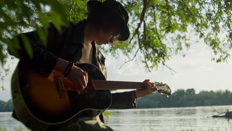 young musician playing acoustic guitar by the river
