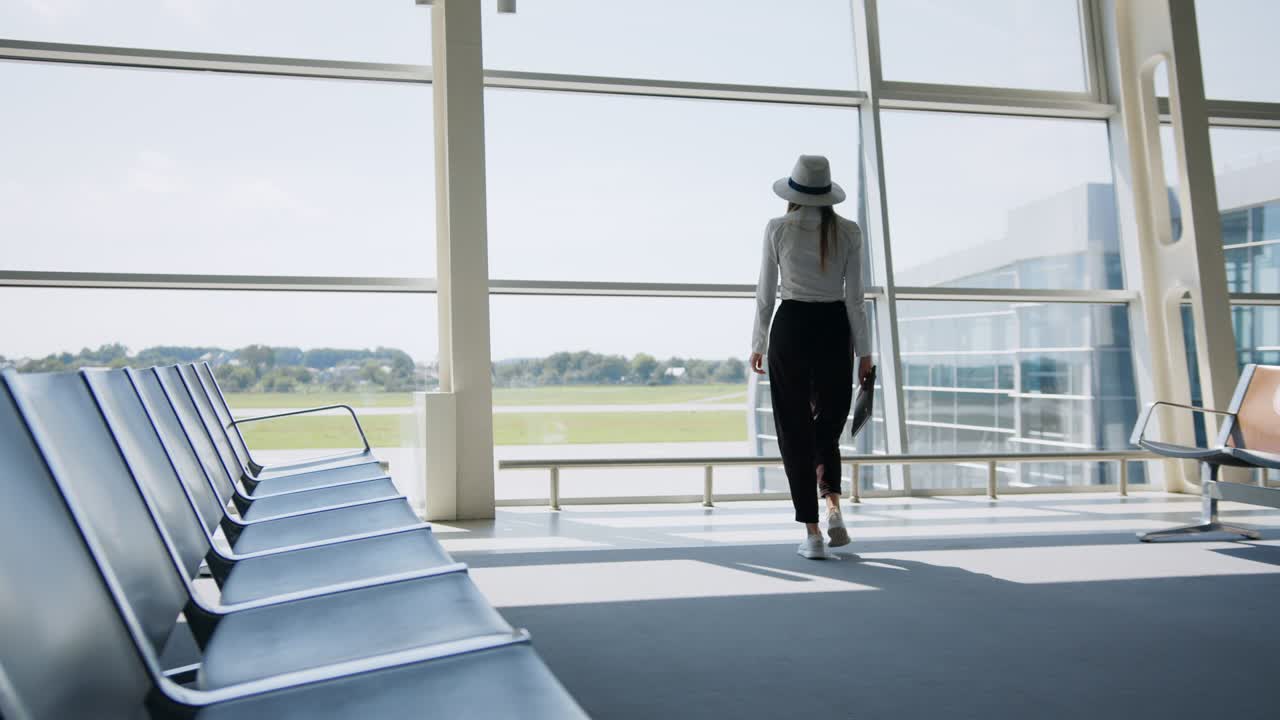 Girl tourist freelancer works and waits for flight in waiting room. Concept travel, remote work. Silhouette against the background of a large window. The concept of work remotely from the office