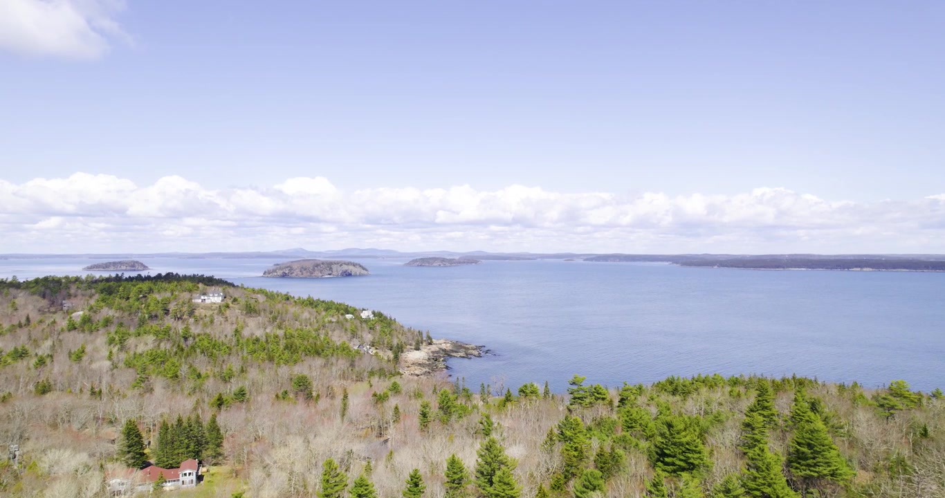 Et bredt luftfoto afslører den barske havkyst med stedsegrønne skove omkring Acadia Maine i klart dagslys.