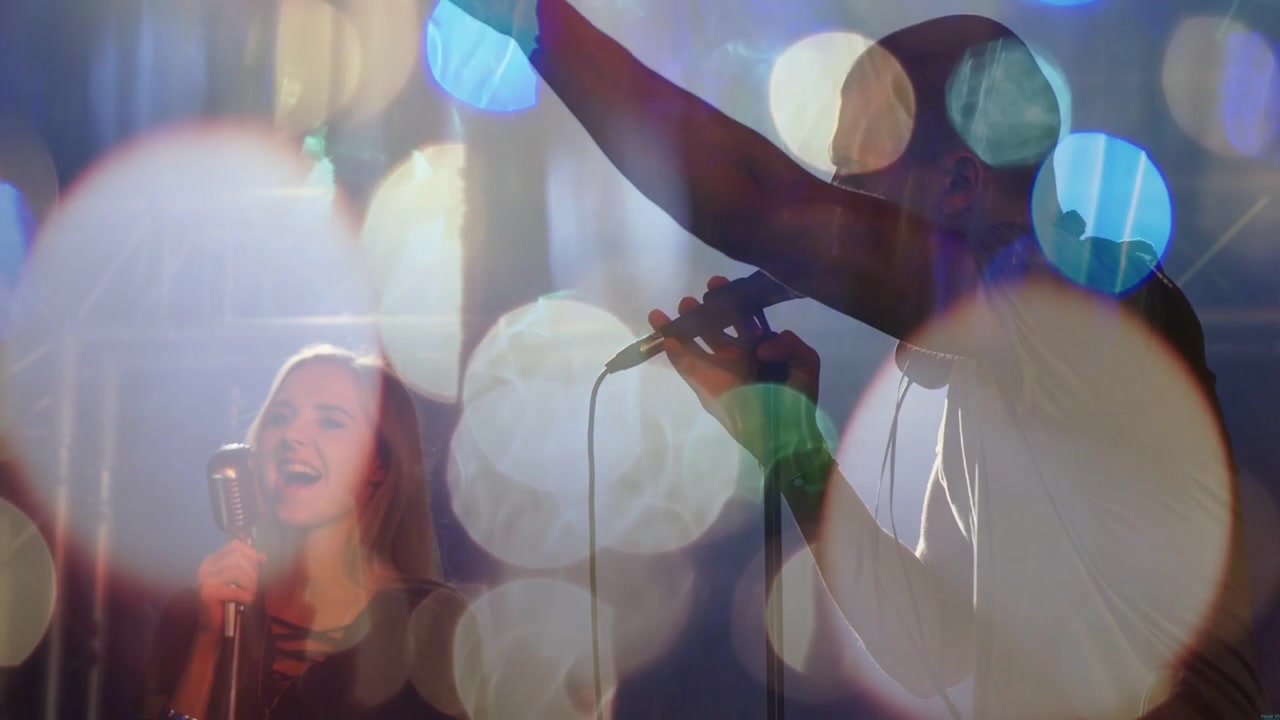 Mandlig sanger begynder at synge, kvindelig sangerinde træder ind og løfter mikrofonen, skaber musik med bokeh-effekt.