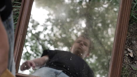 a young high school aged teen boy looking serious, angry and sad looks at his reflection in a mirror