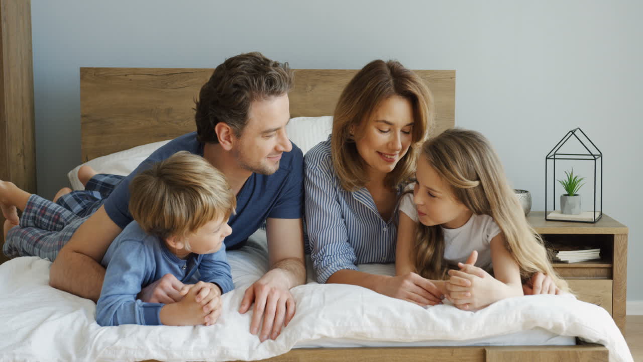 Vídeo Gratis - Padres alegres y sus hijos acostados en la cama y ...