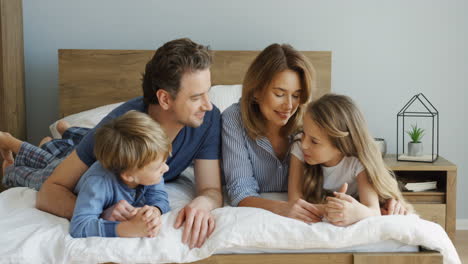 cheerful parents and their sons lying on the bed and talking in the morning