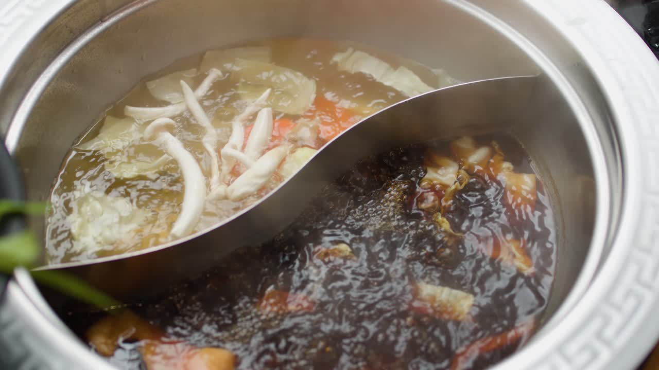 Steaming dual broth hotpot with vegetables and sliced meat added, close-up, overhead view