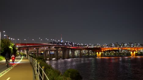 bicyclist on riverbank of han river with seongsu bridge lit up at night