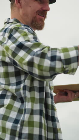 a painter, wearing a black hat and checkered shirt, is captured smiling as he is fully engrossed in his painting. his joy and focus on his creative work are evident in this artistic outdoor scene