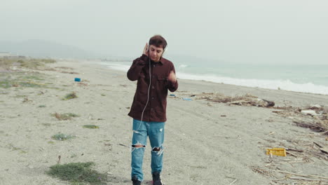young man listening to music on a winter day at the beach near beach