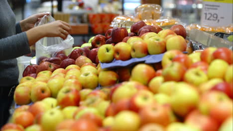 woman in the supermarket putting apples plastic bag