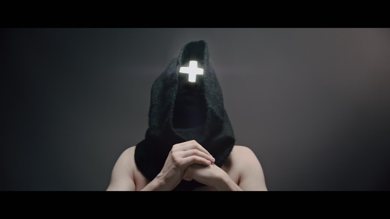 Masked man with cross of light glowing on his face prays
