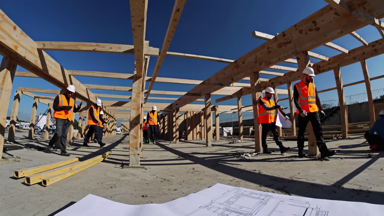 Wide-angle shot of construction workers in safety gear building a wooden structure under a clear