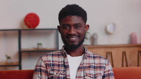 Portrait-of-happy-african-american-teenager-student-guy-smiling,-looking-at-camera-at-home-on-sofa