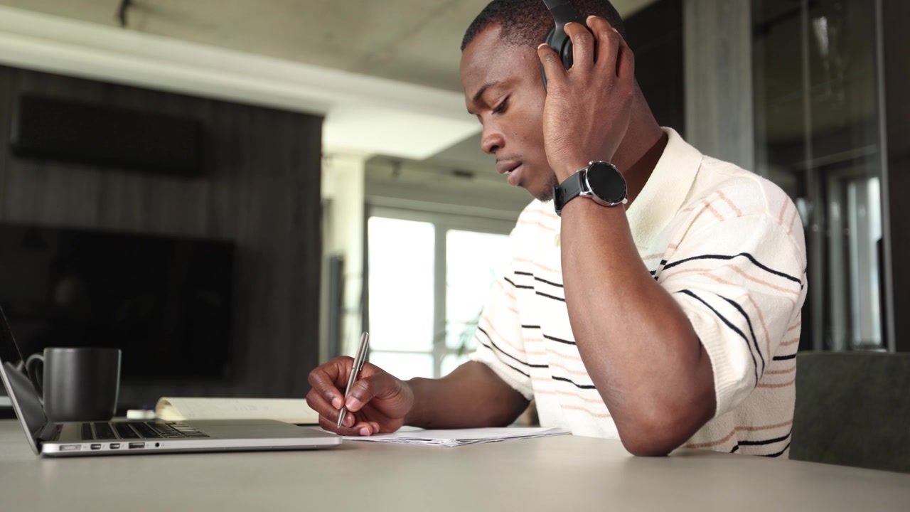 Focused African American Man Writing Notes While Using Laptop