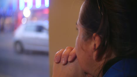 A pensive woman looking out of a cafe window at night.