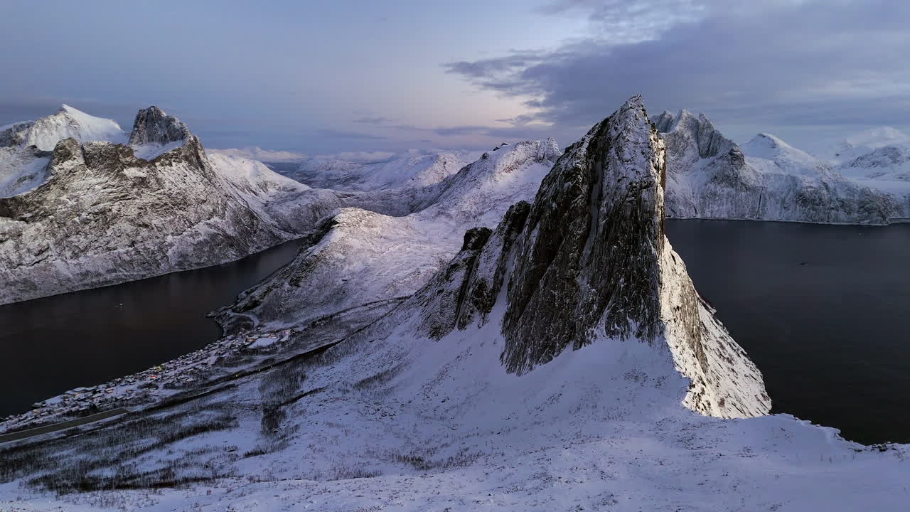 Vista aérea cinematográfica do Pico Segla na Ilha Senja, Noruega, falésias íngremes cobertas de neve acima de fiorde gelado, paisagem ártica dramática com montanhas escarpadas e natureza selvagem invernal