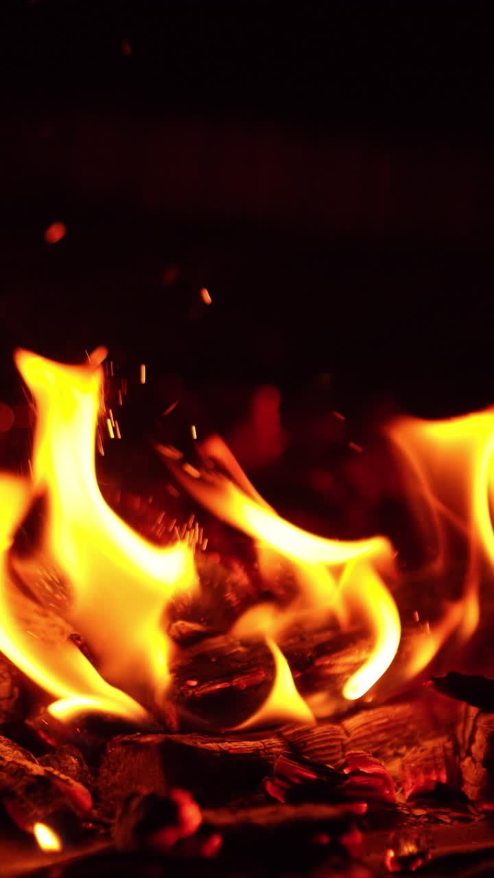 Un bastone colpisce le braci ardenti. Minuscole e numerose scintille volano via. Falò che si spegne. Primo piano. Video verticale