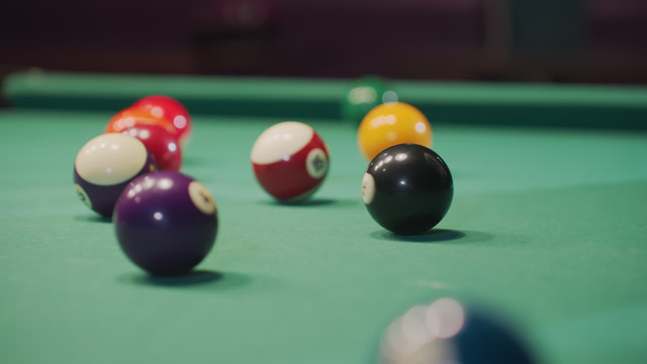 Close-up of hand rolling black billiard ball on green pool table, surrounded by vibrant colorful balls. Focus on precision, movement, and strategy as the game unfolds in a well-lit setting