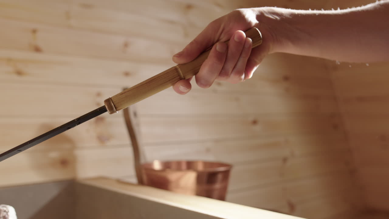 Closeup view of copper ladle pouring water on steaming rocks in wooden sauna