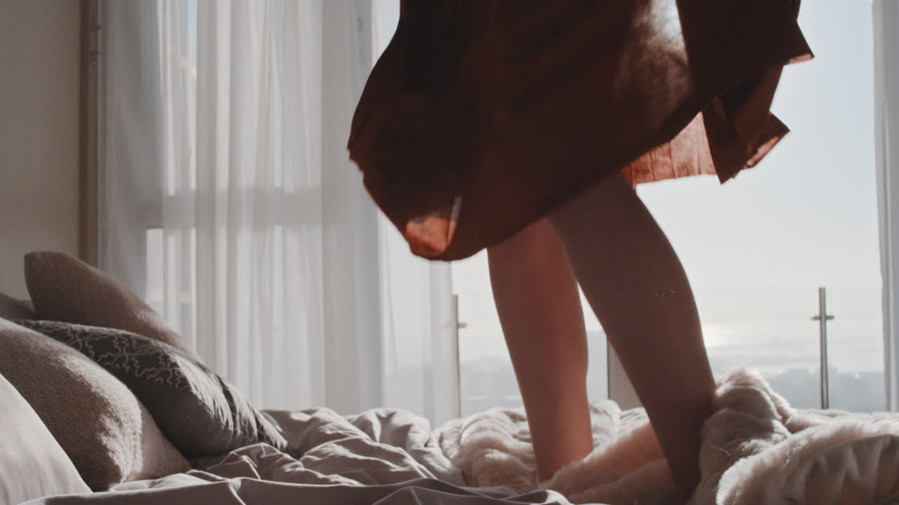 행복한 여성이 호텔 방에서 침대에 뛰어들어 즐거운 성공적인 라이프 스타일을 축하하고 럭셔리 펜트하우스 아파트를 즐기고 있습니다.