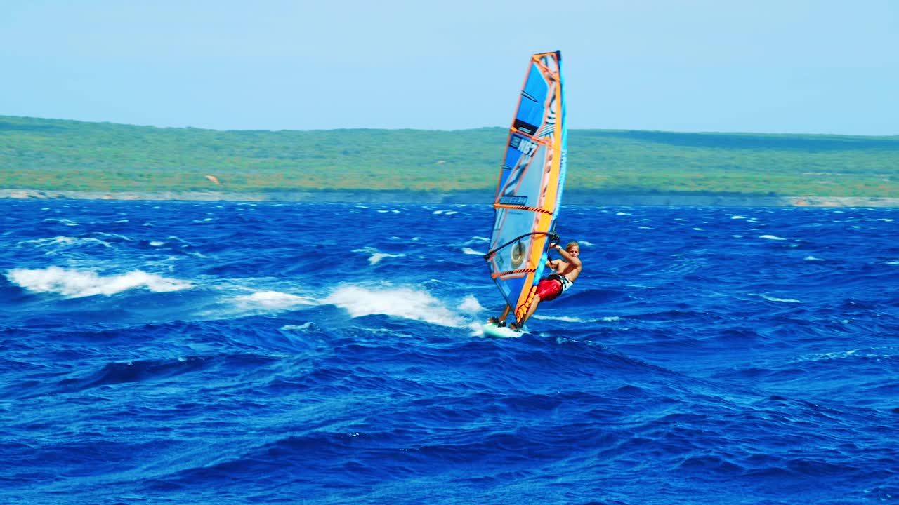 Slow motion shot of a young male windsurfing across the rough and choppy ocean in Bonaire, Caribbean