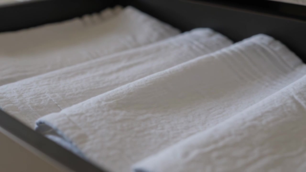 Shifting camera focusing bringing front linen into sharper focus in dark drawer revealing texture