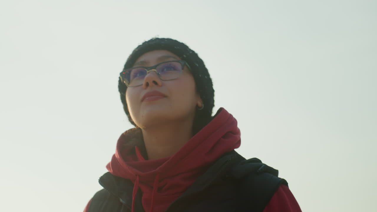 Confident woman with reflective glasses outdoors. Portrait of Asian woman with thoughtful expression outdoors. Closeup image of Asian woman with beanie and scarf gazing upward confidently