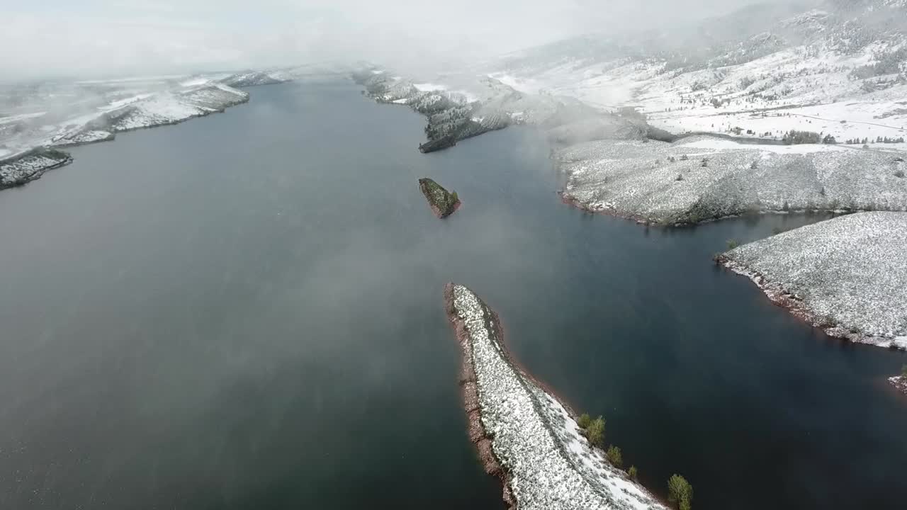 Aerial over foggy lake surrounded by snow covered mountains