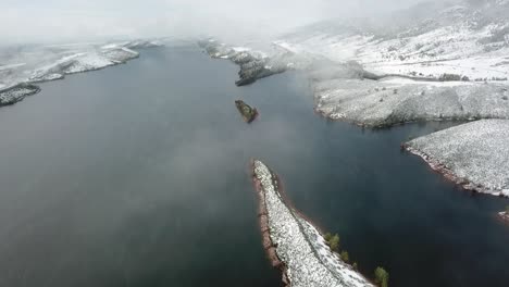 aerial over foggy lake surrounded by snow covered mountains