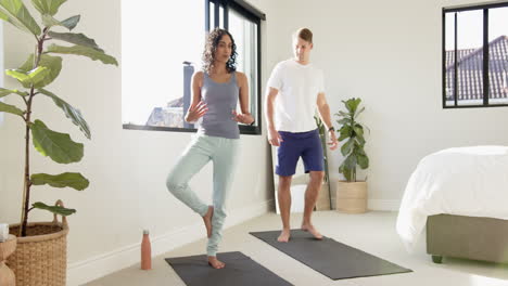 practicing yoga, young multiracial couple balancing on yoga mats in bright bedroom, at home