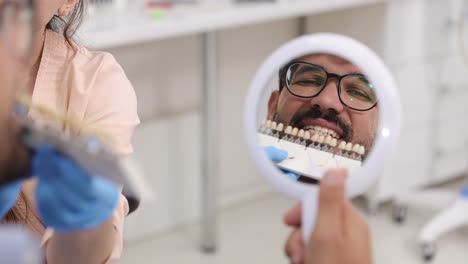 a cheerful patient happily examines his teeth in a dental mirror during an informative consultation with the dentist
