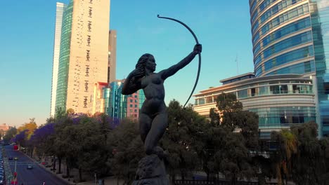 vista de drones estatua de diana cazadora grandes edificios verdes árboles púrpuras en el fondo cielo despejado