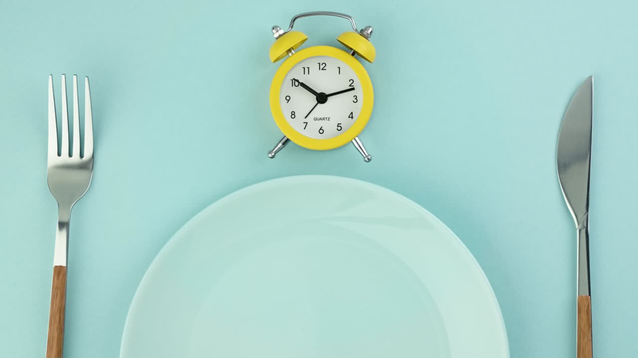 ayuno intermitente, dieta, concepto de la hora del almuerzo. despertador amarillo, plato vacío y cubiertos.