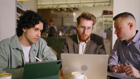 three men in a cafe discussing business over a laptop and tablet